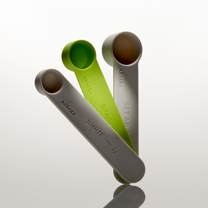 Three ARMRA measuring scoops in gray, lime green, and white with metal bowls and embossed text labels.