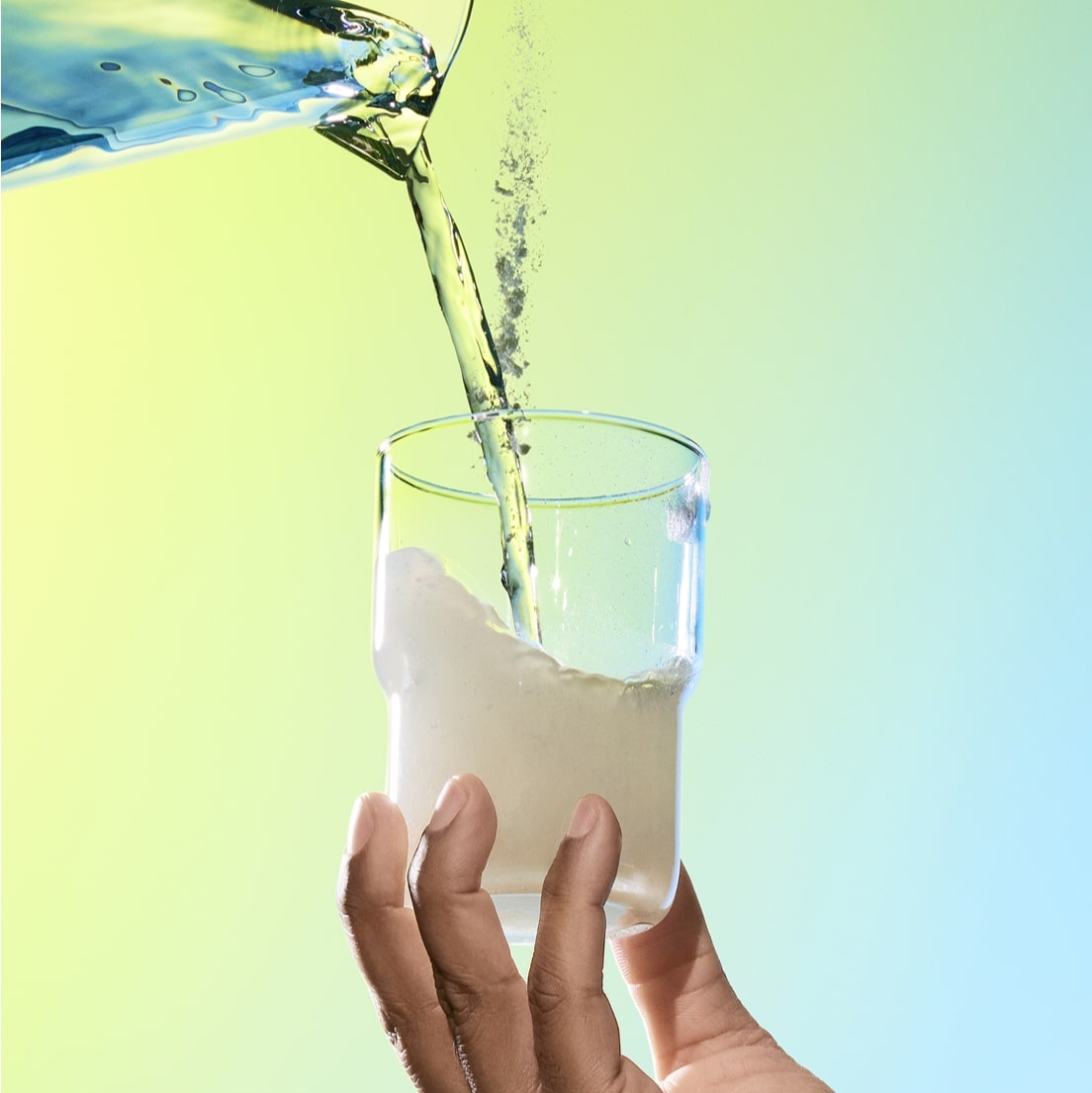 A pitcher of water and a scoop of ARMRA colostrum being poured into a clear glass. 