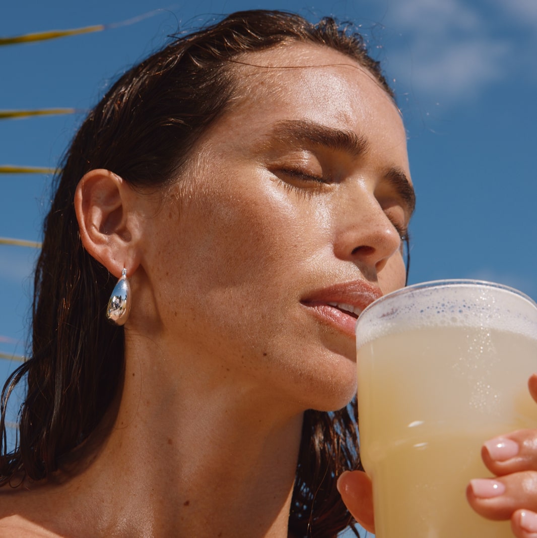 A woman wearing silver earrings holding a glass of ARMRA colostrum