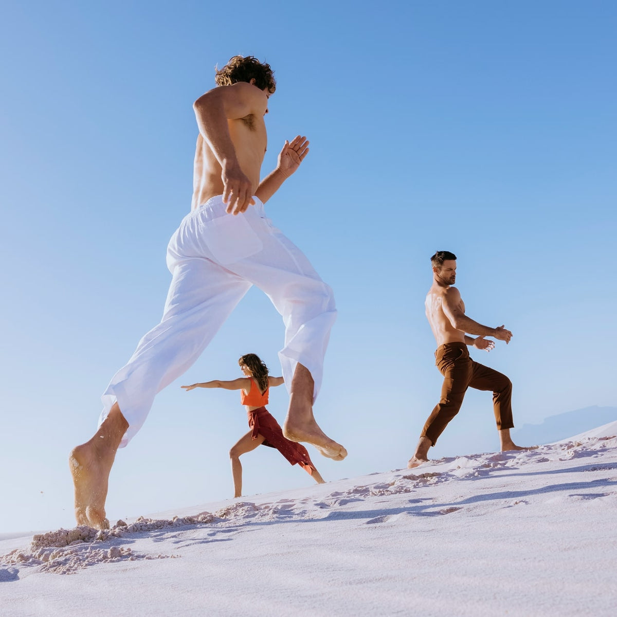 Three active-looking people running on sand 