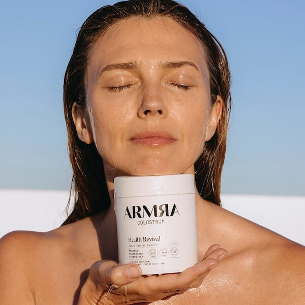 A woman covered in water holding a jar of ARMRA colostrum under her chin