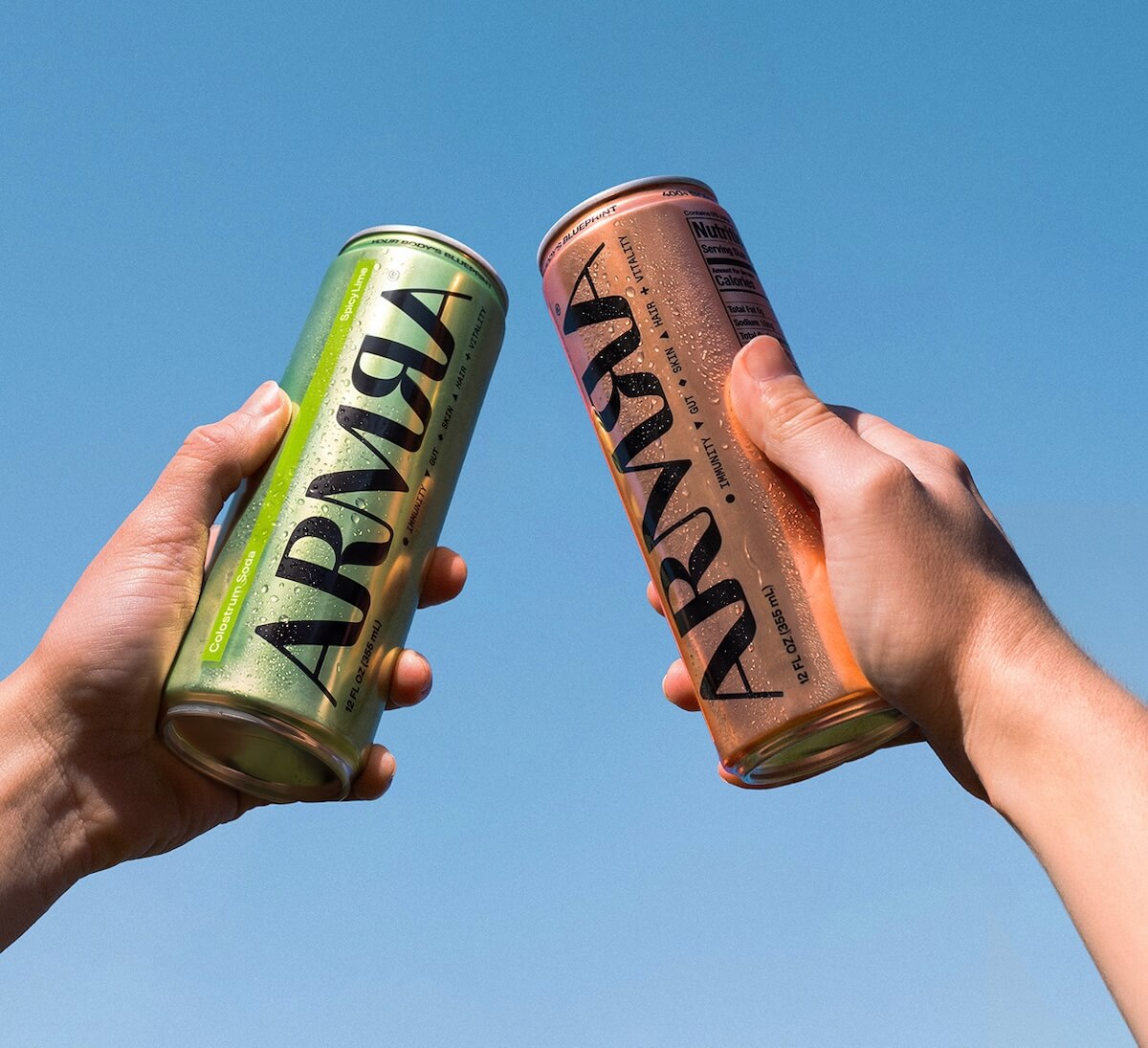 Two people holding up cans of ARMRA Colostrum Soda