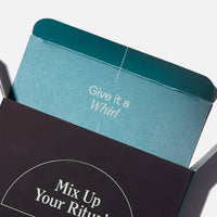 Teal and black product boxes stacked at an angle, with text reading "Give it a Whirl" and "Mix Up Your Ritual."