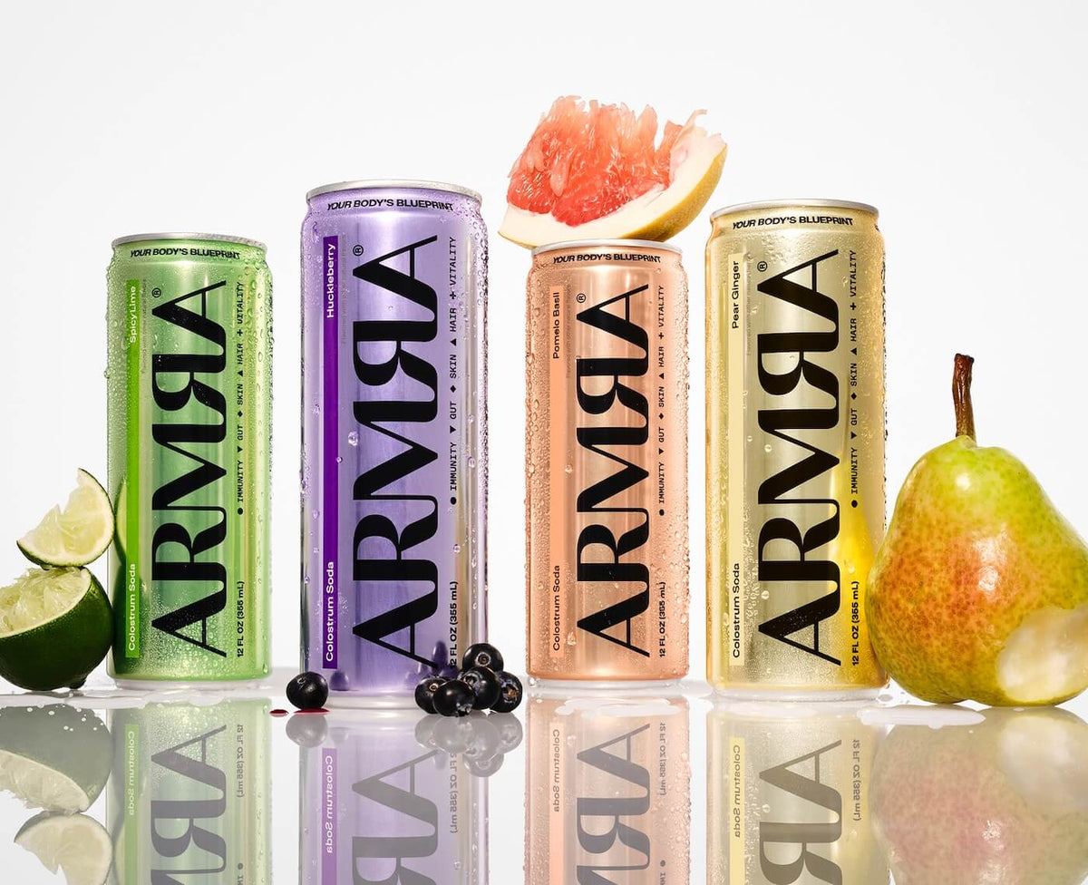 Four ARMRA soda cans in different colors with fruits on a reflective surface.