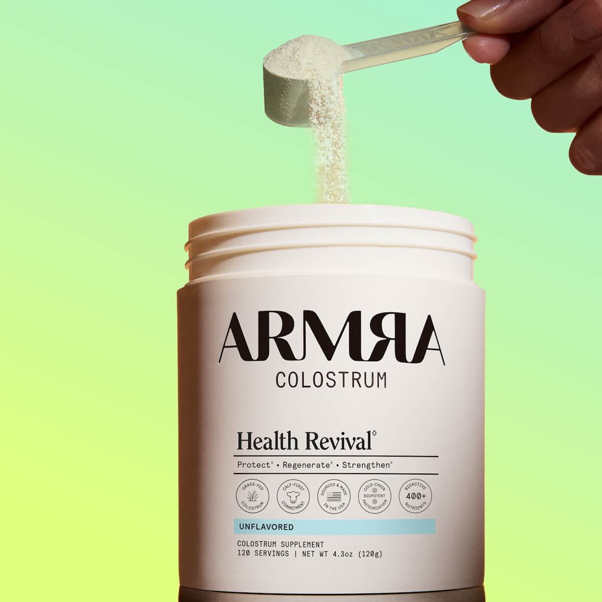 ARMRA Colostrum Health Revival supplement container with a scoop of powder being poured over a green gradient background.