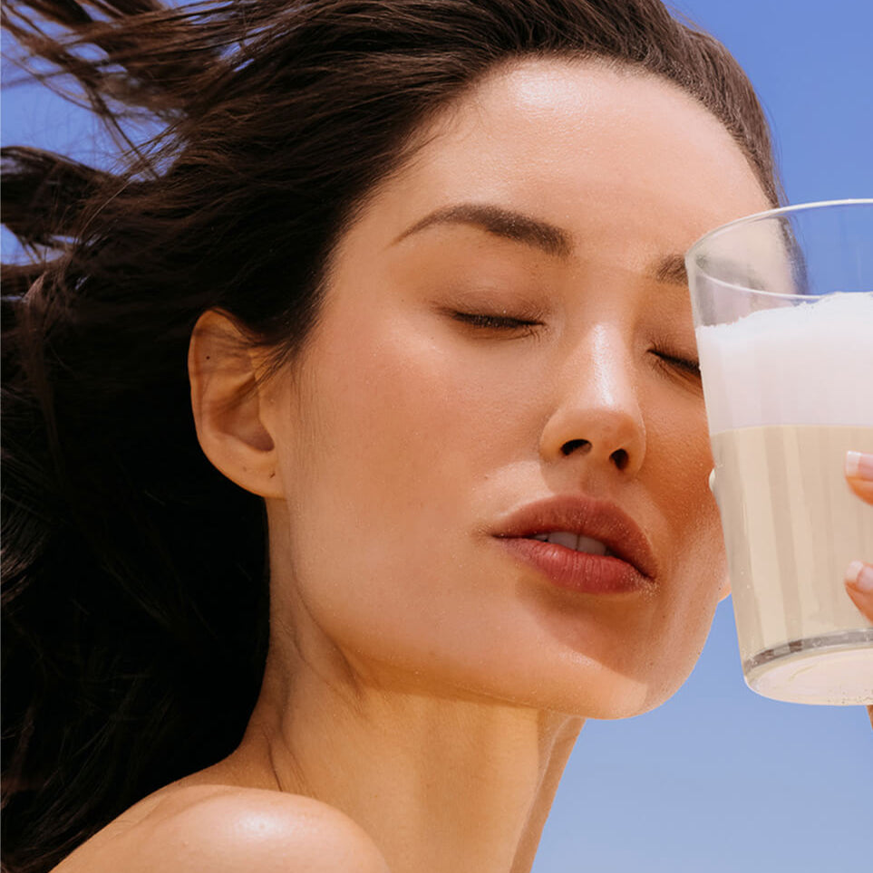 Woman holding a glass of colostrum against a blue sky