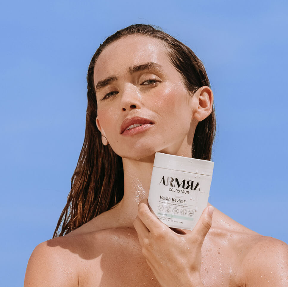 Woman holding ARMRA colostrum against a clear blue sky